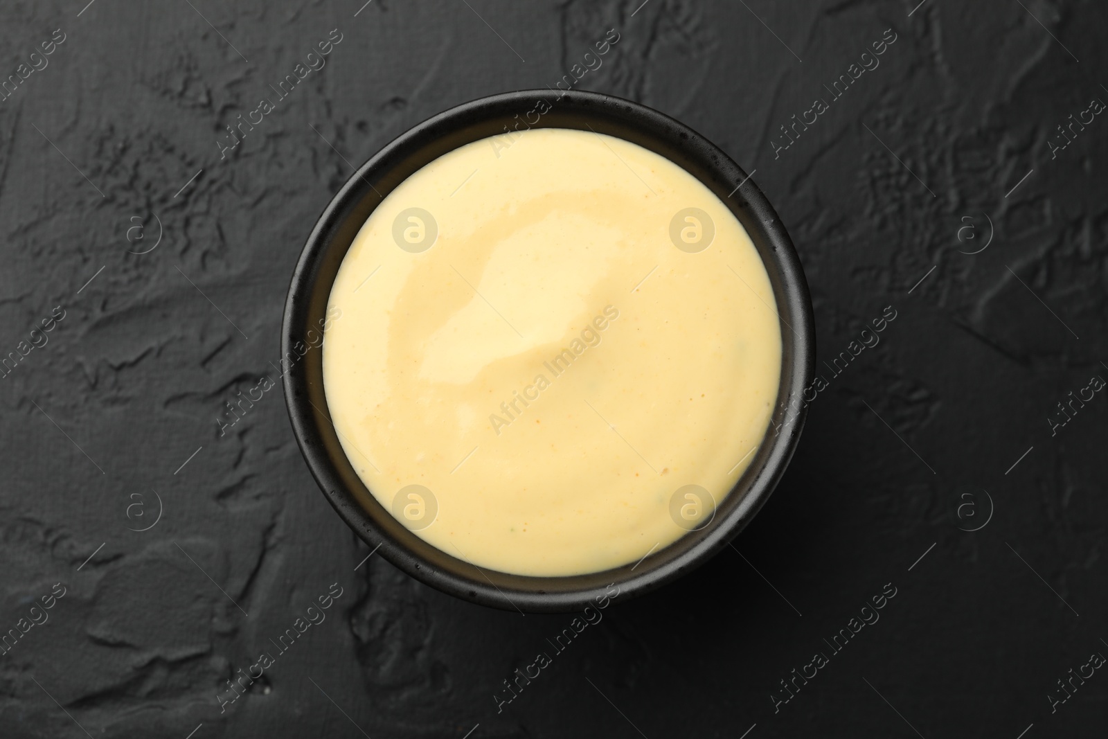 Tasty cheese sauce in bowl on black table, top view Photo of Tasty cheese sauce in bowl on black table, top view