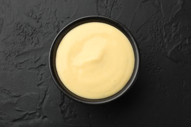 Photo of Tasty cheese sauce in bowl on black table, top view
