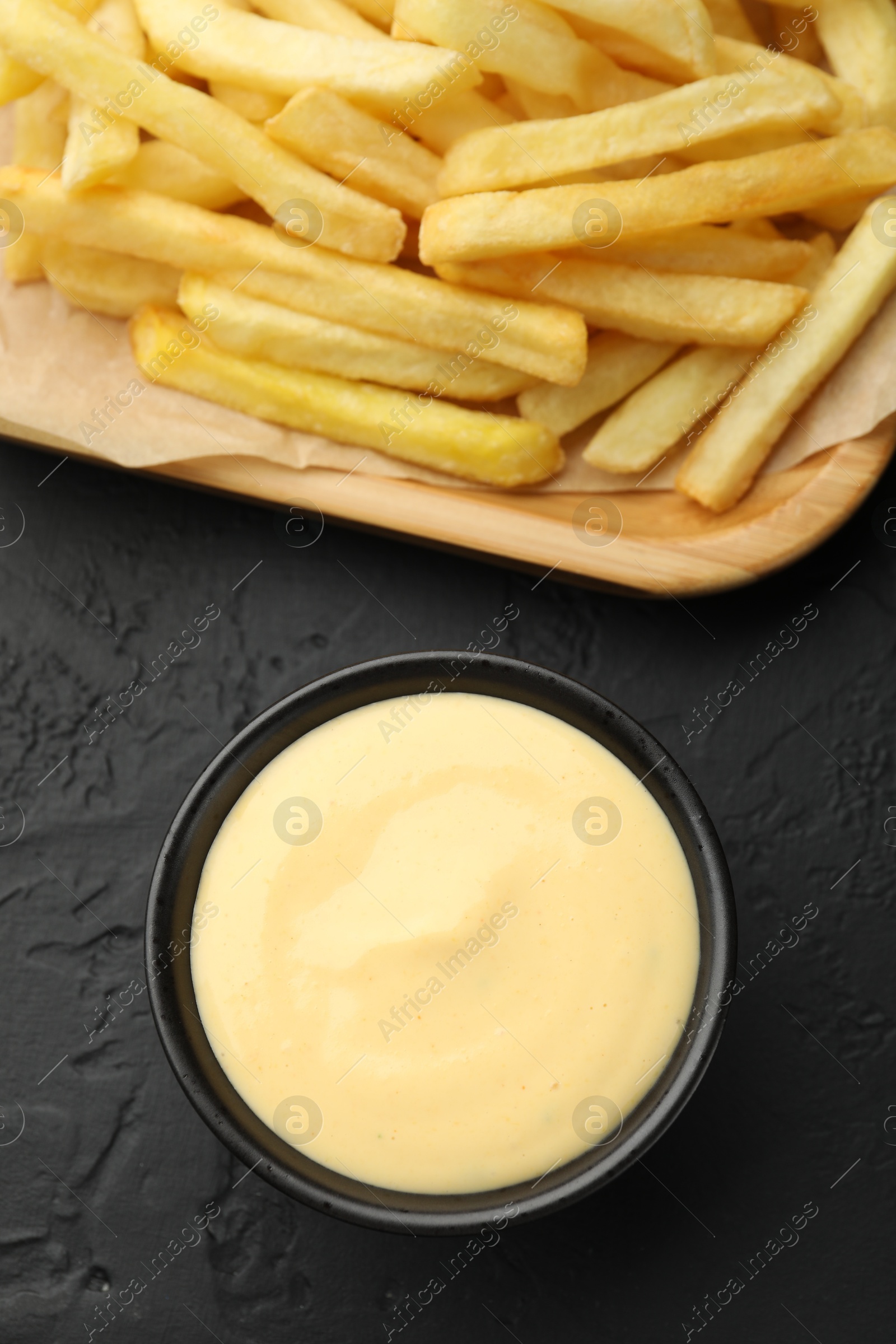 Tasty cheese sauce in bowl and French fries on black table, flat lay Photo of Tasty cheese sauce in bowl and French fries on black table, flat lay