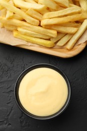 Photo of Tasty cheese sauce in bowl and French fries on black table, flat lay