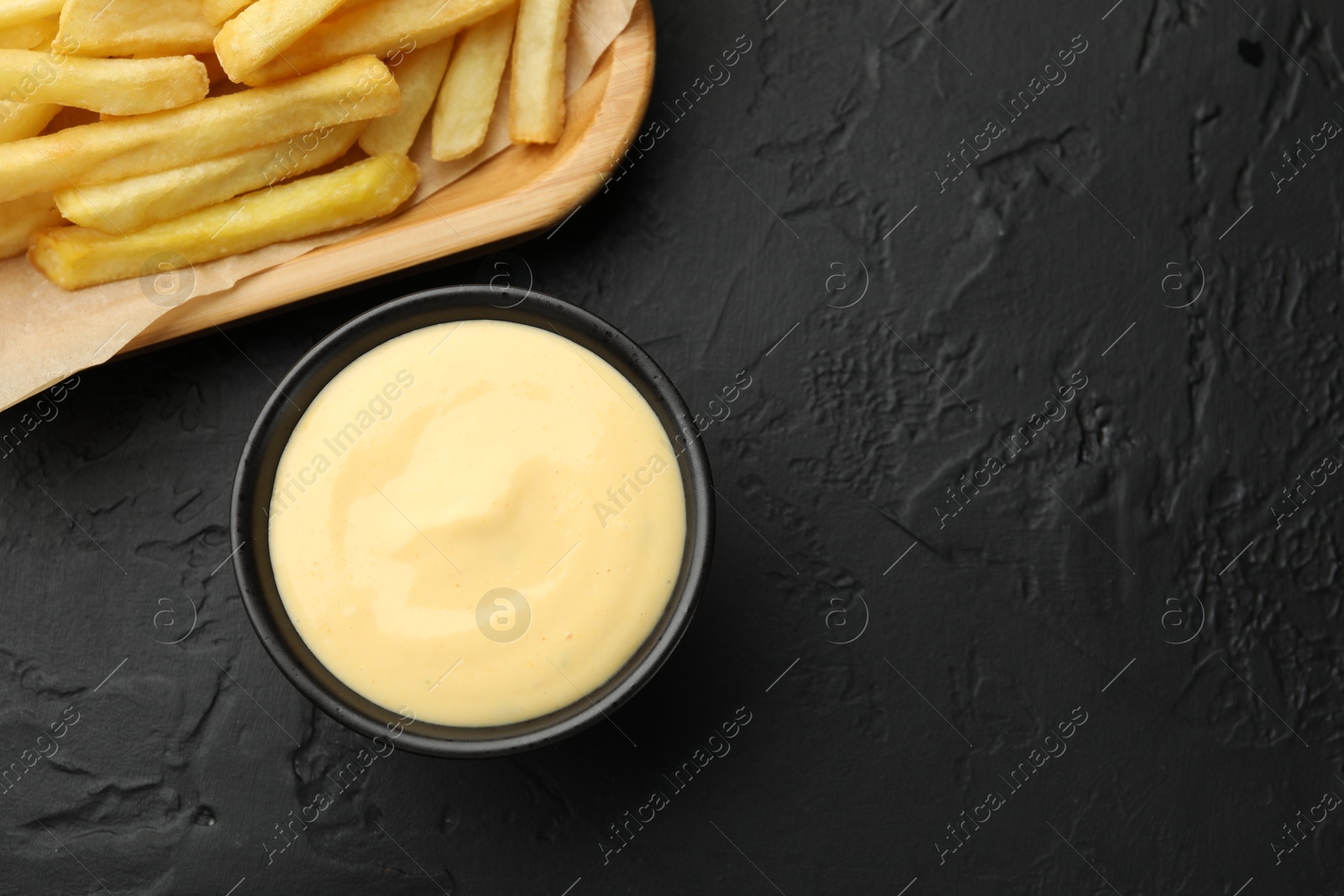 Tasty cheese sauce in bowl and French fries on black table, flat lay. Space for text Photo of Tasty cheese sauce in bowl and French fries on black table, flat lay. Space for text