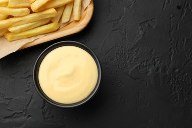 Photo of Tasty cheese sauce in bowl and French fries on black table, flat lay. Space for text