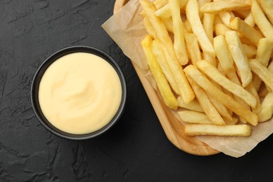 Photo of Tasty cheese sauce in bowl and French fries on black table, flat lay