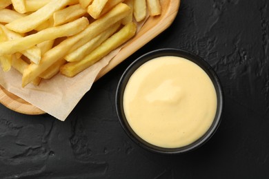 Photo of Tasty cheese sauce in bowl and French fries on black table, flat lay