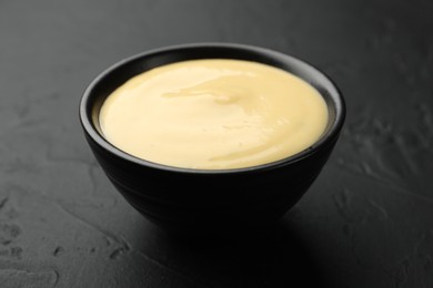 Photo of Tasty cheese sauce in bowl on black table, closeup