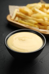 Photo of Tasty cheese sauce in bowl and French fries on black table, closeup