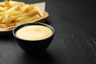 Photo of Tasty cheese sauce in bowl and French fries on black table, closeup. Space for text