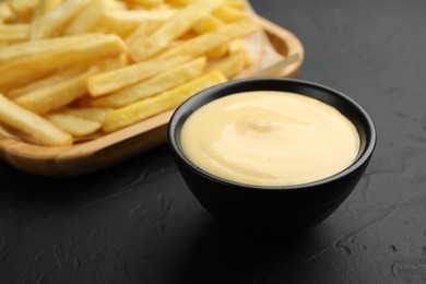 Photo of Tasty cheese sauce in bowl and French fries on black table, closeup