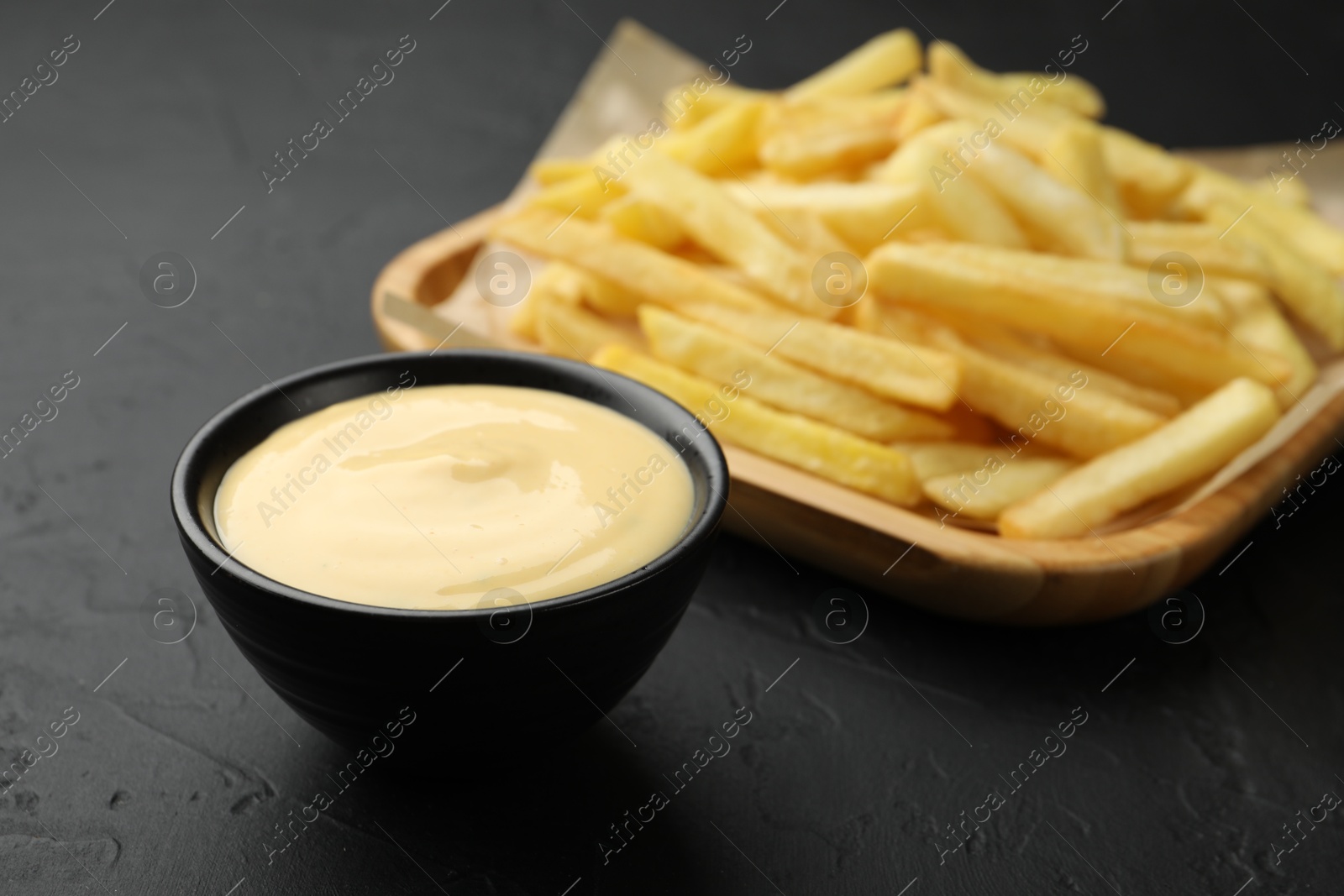 Tasty cheese sauce in bowl and French fries on black table, closeup Photo of Tasty cheese sauce in bowl and French fries on black table, closeup