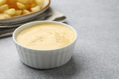 Photo of Tasty cheese sauce in bowl and French fries on grey table, closeup. Space for text