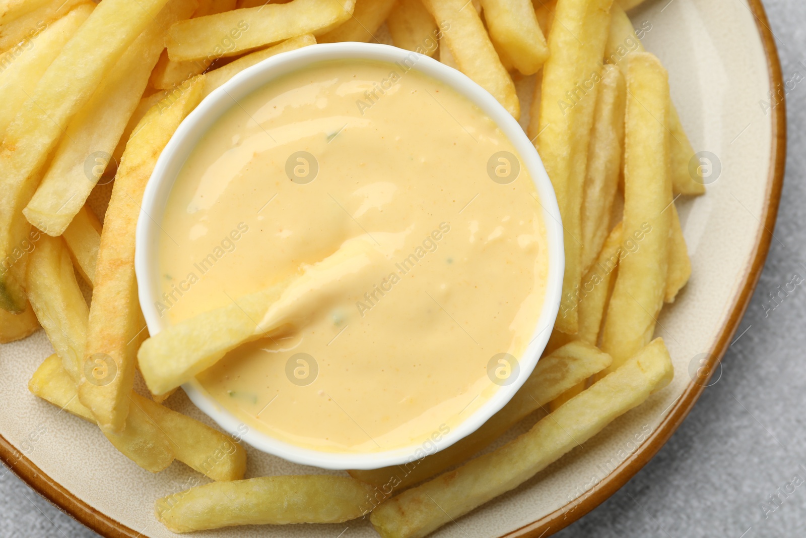 Tasty cheese sauce in bowl and French fries on grey table, top view Photo of Tasty cheese sauce in bowl and French fries on grey table, top view