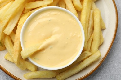 Photo of Tasty cheese sauce in bowl and French fries on grey table, top view