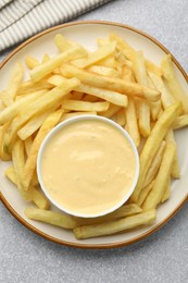 Photo of Tasty cheese sauce in bowl and French fries on grey table, top view