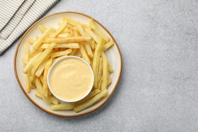 Photo of Tasty cheese sauce in bowl and French fries on grey table, top view. Space for text