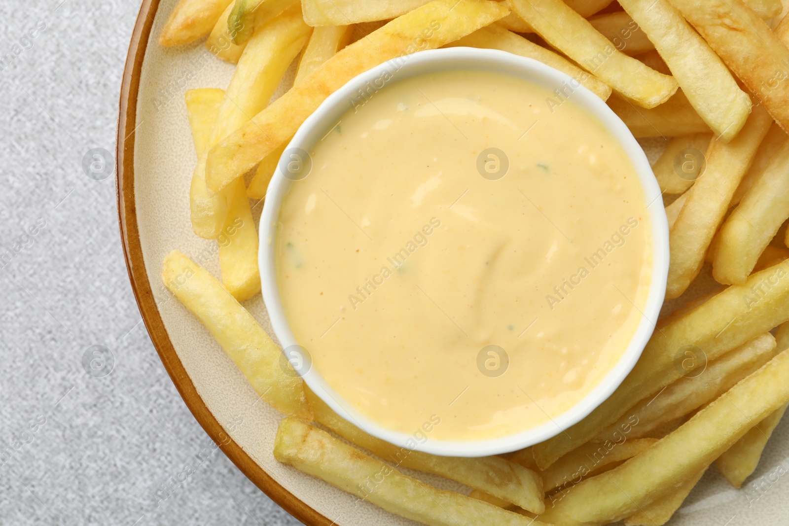 Tasty cheese sauce in bowl and French fries on grey table, top view Photo of Tasty cheese sauce in bowl and French fries on grey table, top view