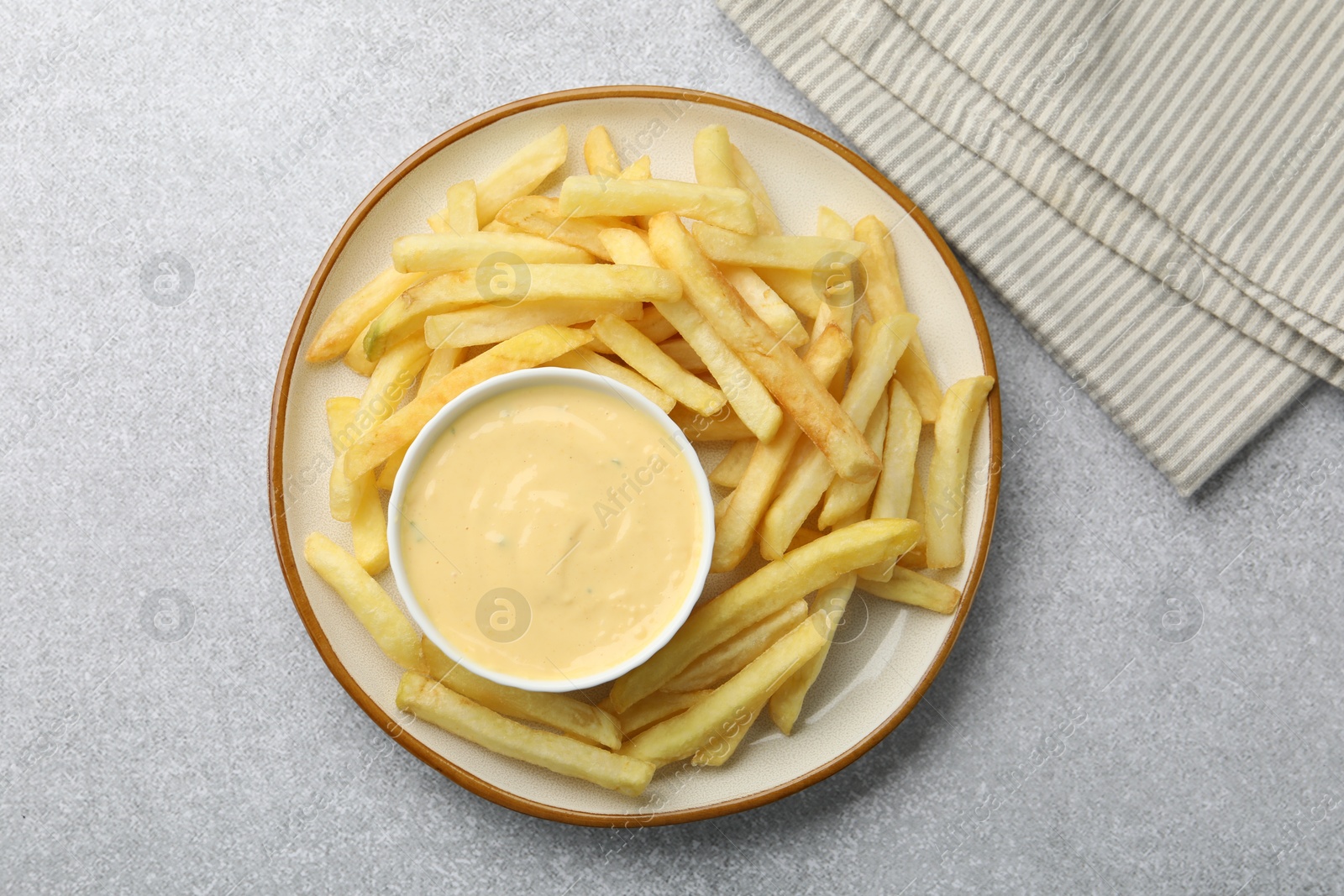 Tasty cheese sauce in bowl and French fries on grey table, top view Photo of Tasty cheese sauce in bowl and French fries on grey table, top view