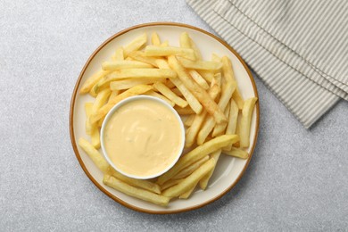 Photo of Tasty cheese sauce in bowl and French fries on grey table, top view