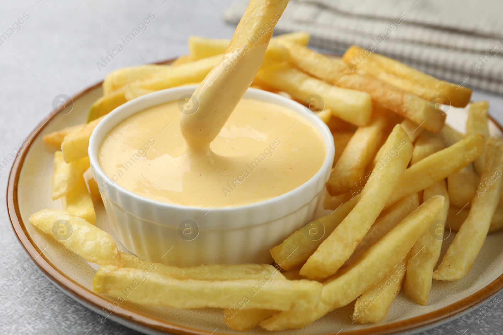 Dipping French fry into cheese sauce at grey table, closeup Photo of Dipping French fry into cheese sauce at grey table, closeup