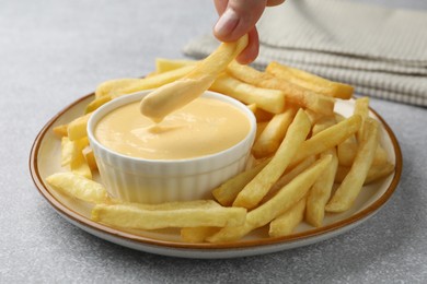 Photo of Woman dipping French fry into cheese sauce at grey table, closeup