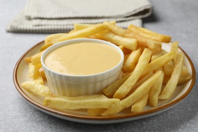 Photo of Tasty cheese sauce in bowl and French fries on grey table, closeup