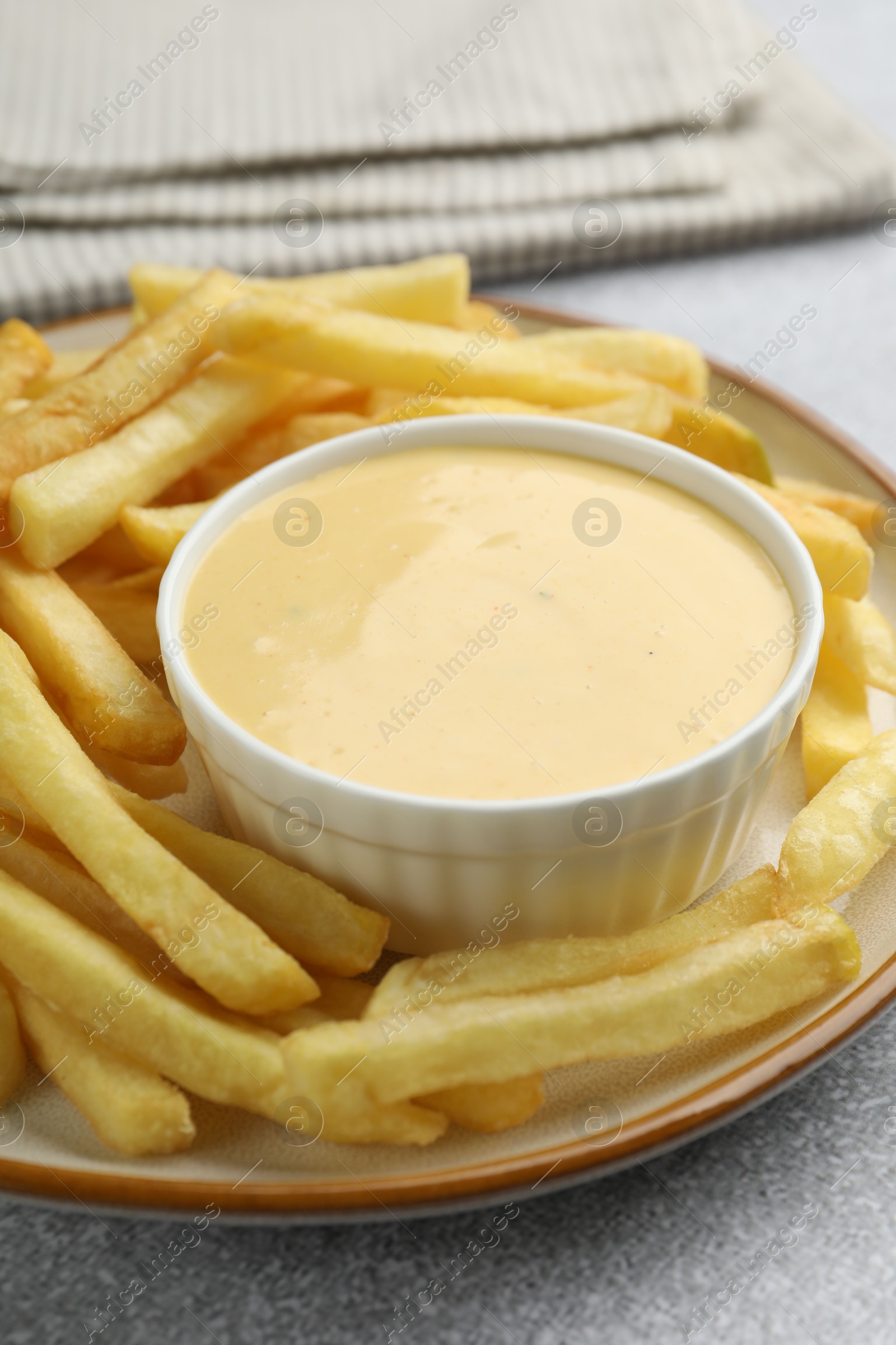 Tasty cheese sauce in bowl and French fries on grey table, closeup Photo of Tasty cheese sauce in bowl and French fries on grey table, closeup