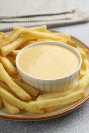 Photo of Tasty cheese sauce in bowl and French fries on grey table, closeup