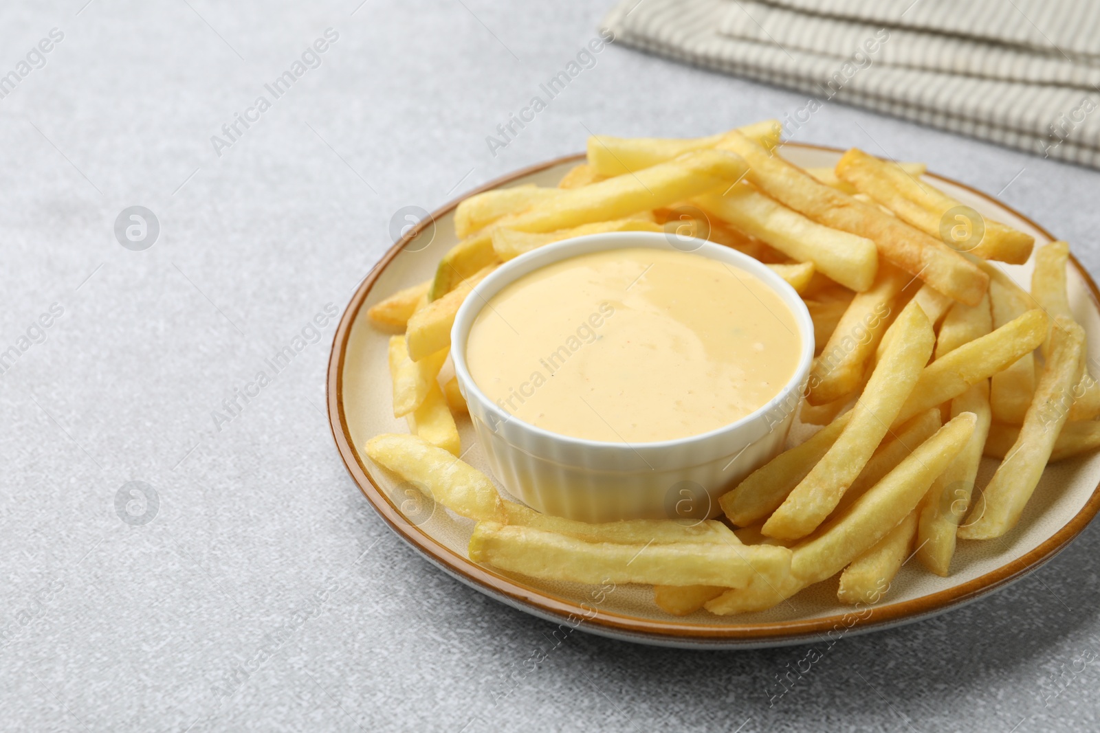 Tasty cheese sauce in bowl and French fries on grey table, closeup. Space for text Photo of Tasty cheese sauce in bowl and French fries on grey table, closeup. Space for text