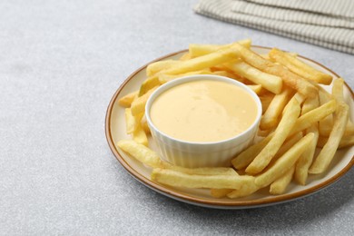 Photo of Tasty cheese sauce in bowl and French fries on grey table, closeup. Space for text