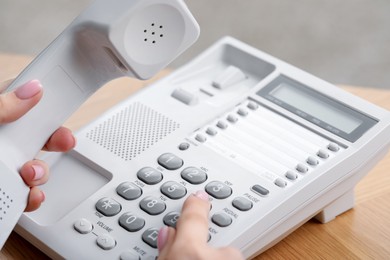 Photo of Woman dialing number on telephone at wooden table against blurred background, closeup