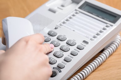 Photo of Woman dialing number on telephone at wooden table, closeup