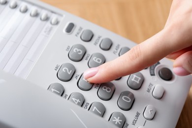 Photo of Woman dialing number on telephone at table, closeup