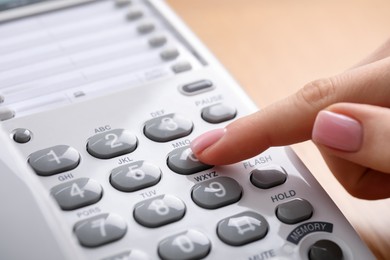 Photo of Woman dialing number on telephone against blurred background, closeup