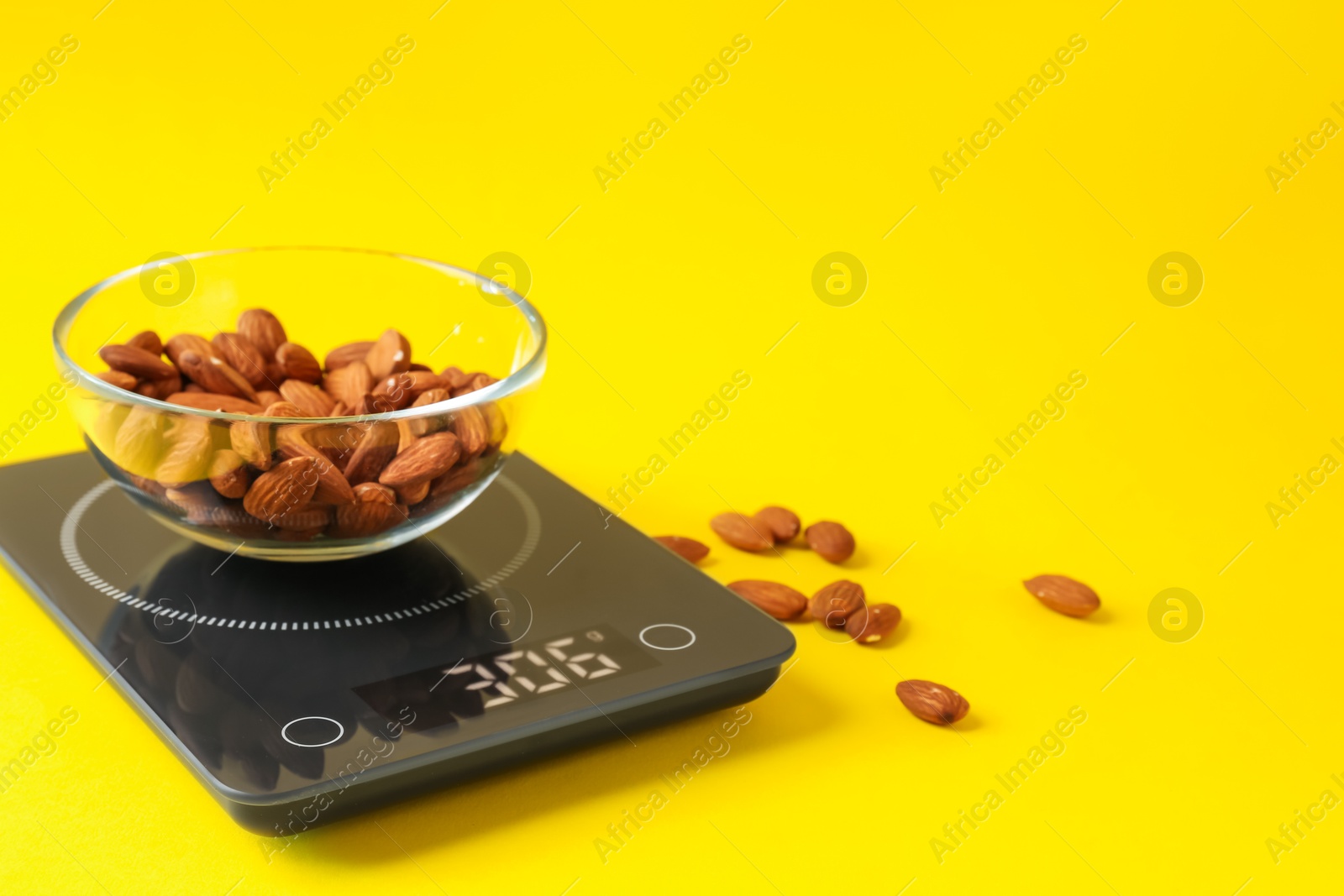Electronic kitchen scale with bowl of almond nuts on yellow background, closeup. Space for text Photo of Electronic kitchen scale with bowl of almond nuts on yellow background, closeup. Space for text