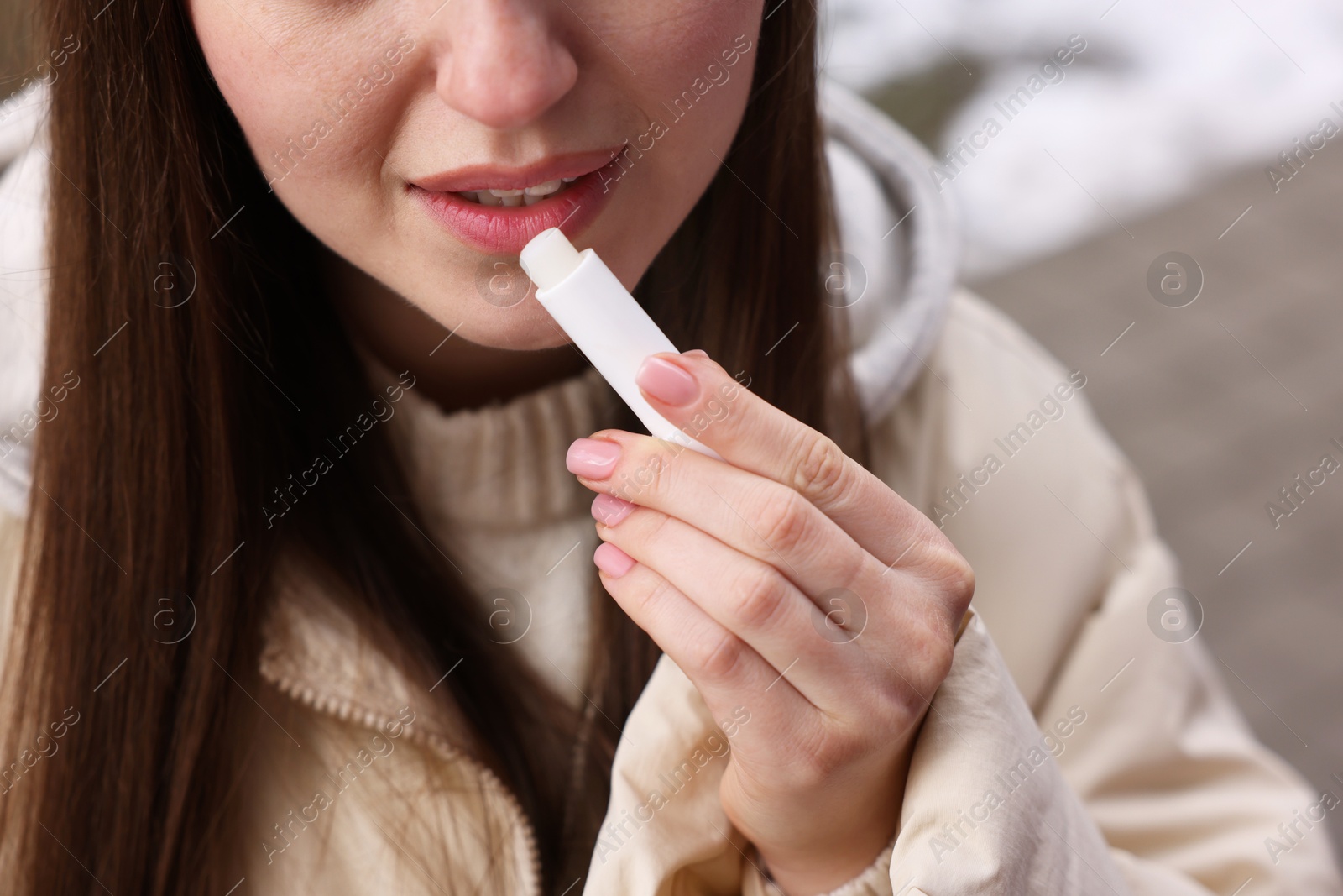 Photo of Young woman applying lip balm outdoors, closeup