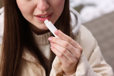 Photo of Young woman applying lip balm outdoors, closeup