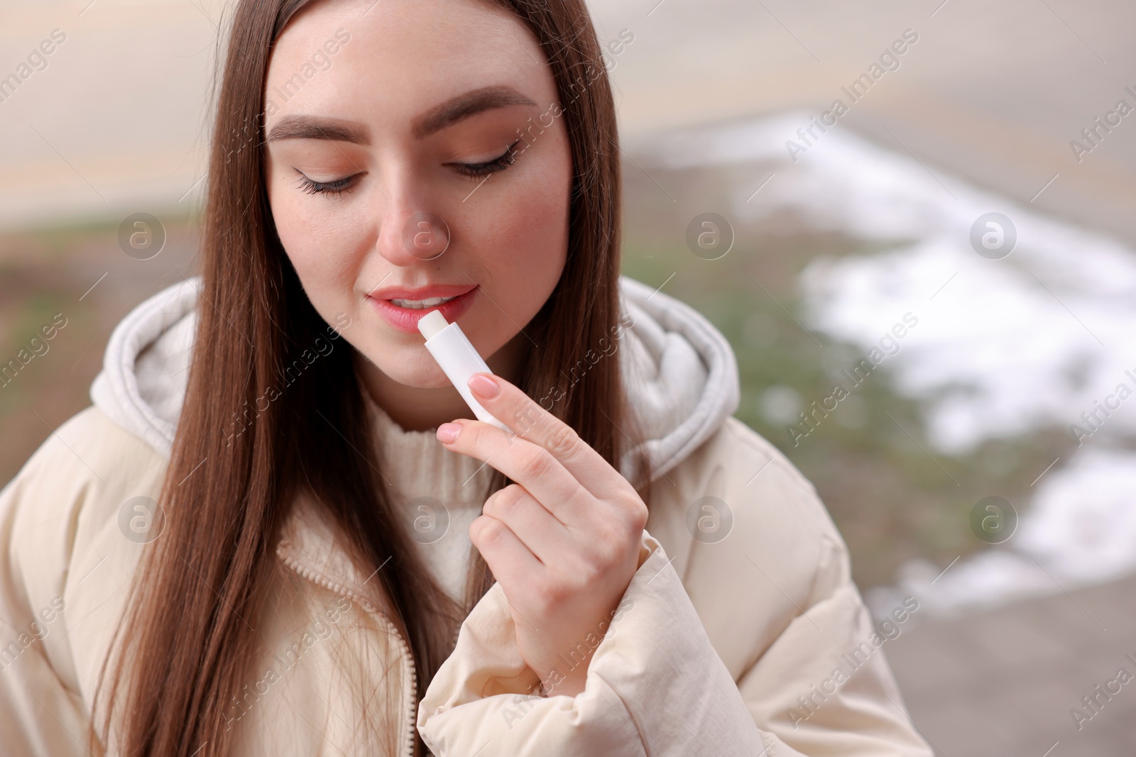 Photo of Beautiful young woman applying lip balm on winter day