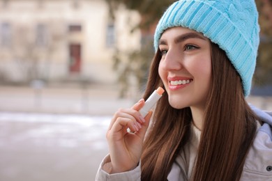 Photo of Beautiful young woman applying lip balm on winter day. Space for text