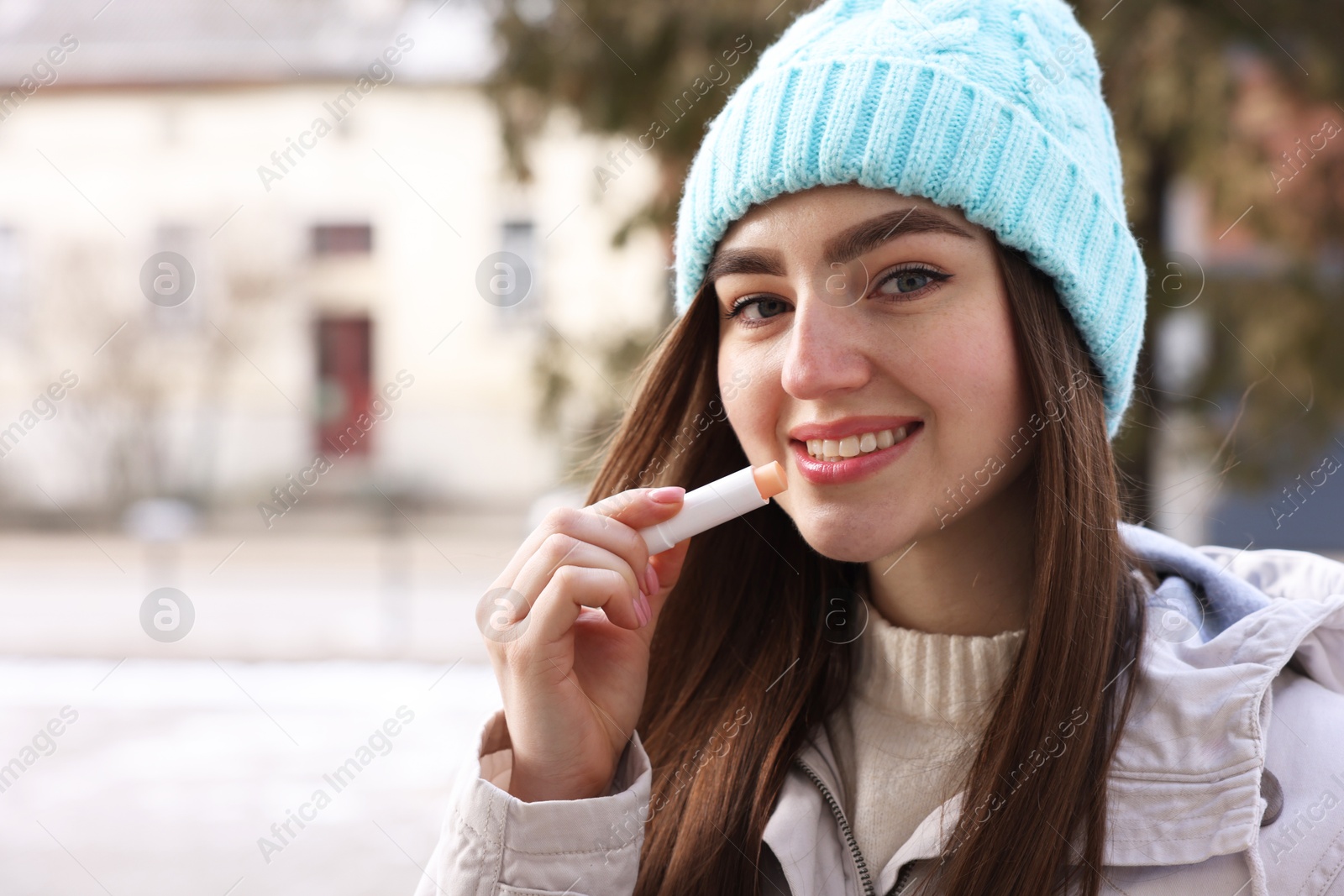 Photo of Beautiful young woman applying lip balm on winter day. Space for text