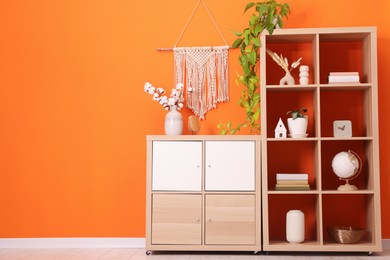 Photo of Wooden shelving unit with different home decor and houseplant near orange wall indoors, space for text