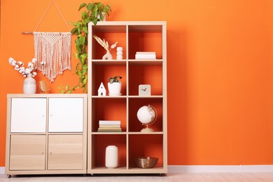 Photo of Wooden shelving unit with different home decor and houseplant near orange wall indoors, space for text