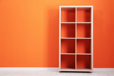 Photo of Empty wooden shelving unit near orange wall indoors, space for text