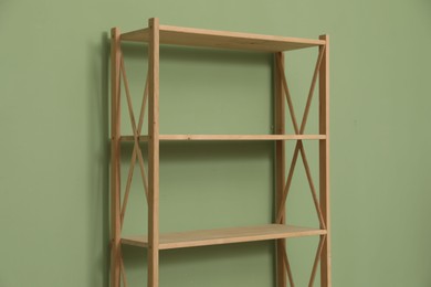 Photo of Empty wooden shelving unit near olive wall indoors