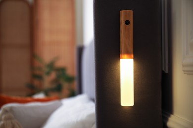 Photo of Glowing modern LED lamp on bed indoors, closeup