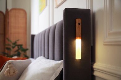 Photo of Glowing modern LED lamp on bed indoors, closeup