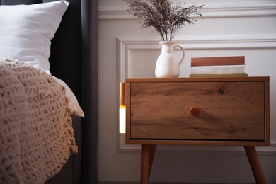 Photo of Glowing modern LED lamp on wooden bedside table indoors