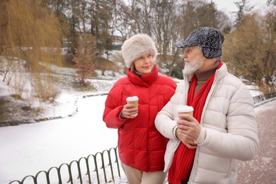 Photo of Lovely senior couple with paper cups walking at winter park. Space for text