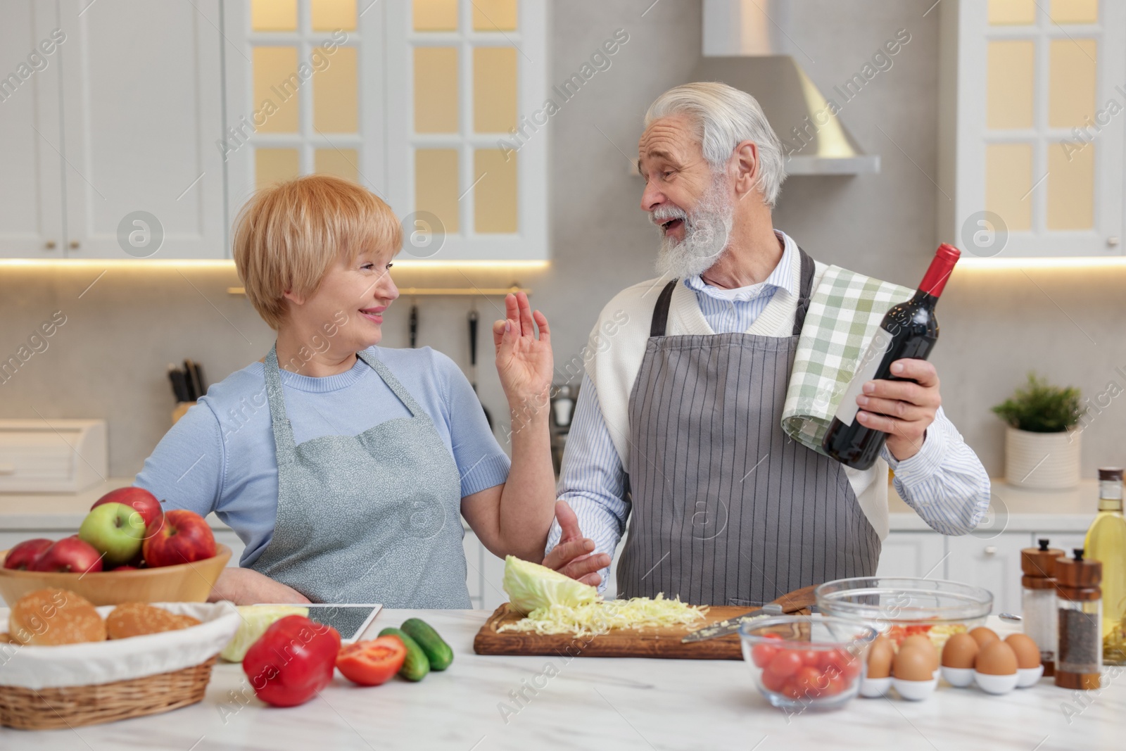 Photo of Senior man suggesting wine to his wife while cooking in kitchen