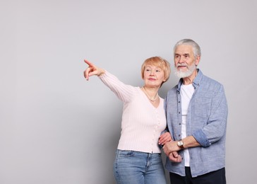 Photo of Lovely senior couple. Woman pointing at something to her husband on grey background. Space for text