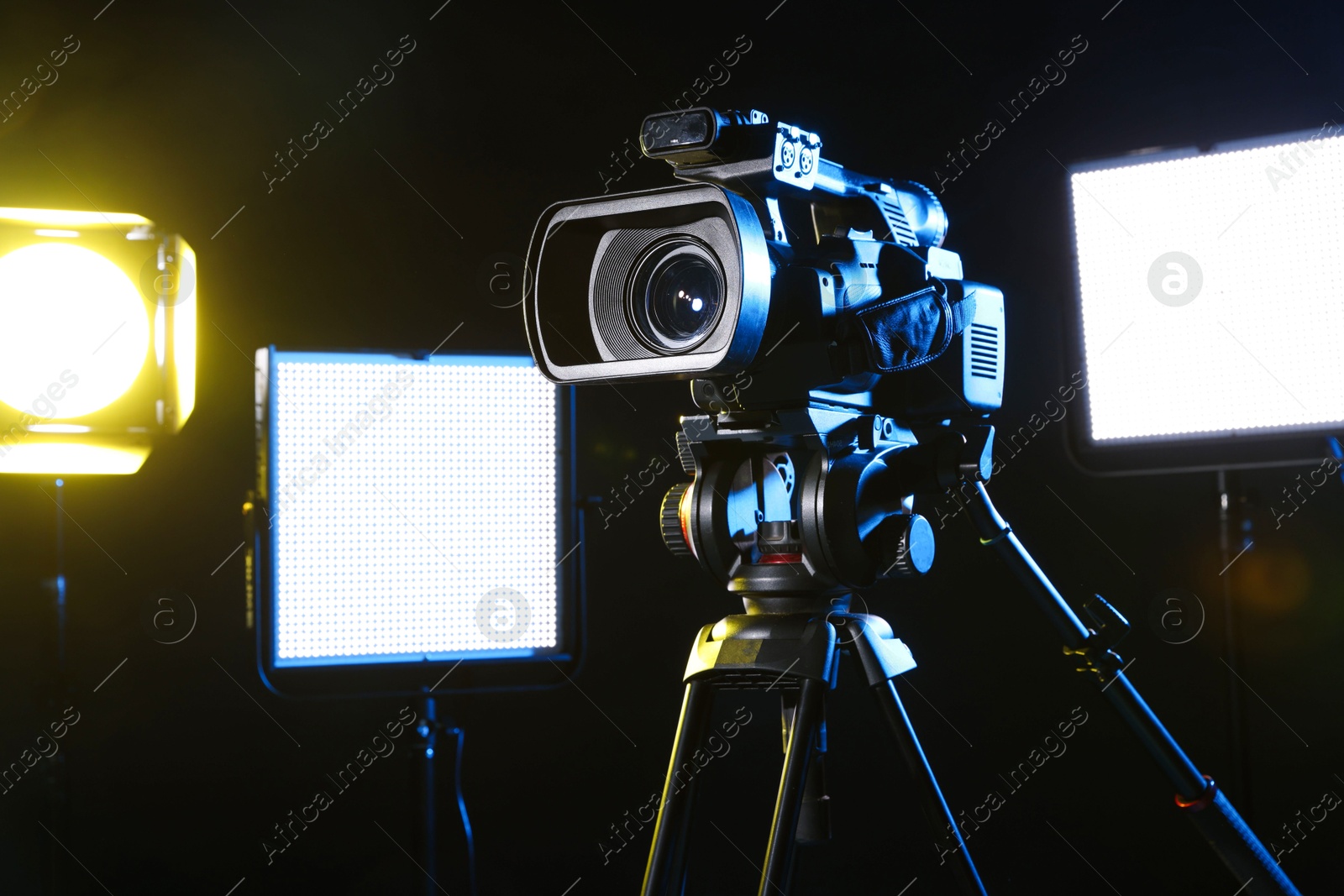 Photo of Modern video camera with tripod and lighting equipment on black background