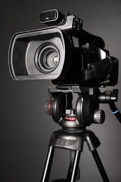 Photo of Modern video camera with tripod on grey background, closeup